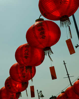 View up of tags, inscribed with wishes, dangling from red, paper lanterns, hung in a row outside the Goddess of Mercy Temple.