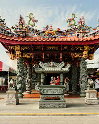 Green and yellow dragons dance on a red pagoda roof hanging with gilt lanterns at the Chew Jetty entrance temple in Penang.