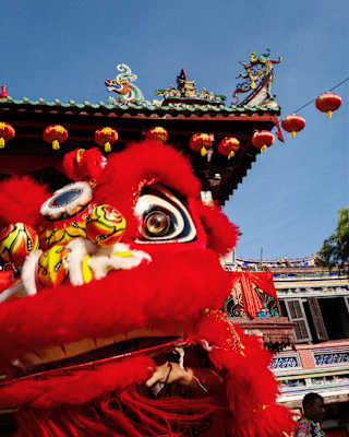 Low-angle view of Cheah Kongsi obstructed by a large furry red lion head being held aloft during the customary Lion Dance.