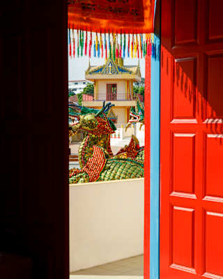 View from inside, past an open red door to a walkway overlooking a majestic temple dragon in shiny red, green and blue tiles.
