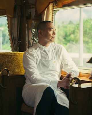 Chef André Chiang, in chef whites, sits at a wooden counter in the bronze-toned L'Oriental Car, gazing out of the window.