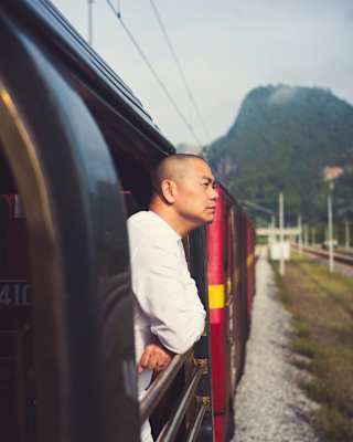 Chef André Chiang leans on the rails of an open-sided carriage, looking out, in an external shot along the side of the train.