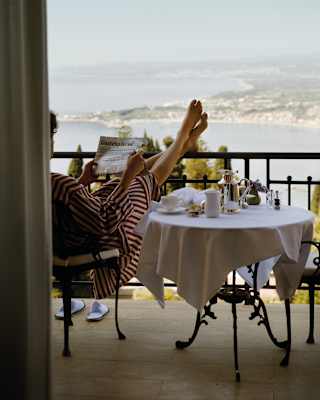 Lady in a red striped dress relaxing over breakfast with her bare feet rested on a balcony railing