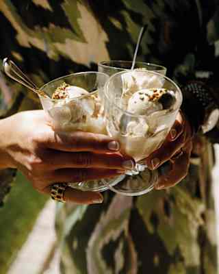 Close-up of a lady's hands clasping three glasses filled with gelato and topped with chopped nuts