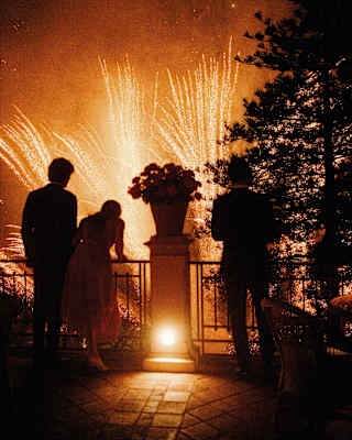 Three people watching fireworks from The Grand Hotel Timeo's balcony
