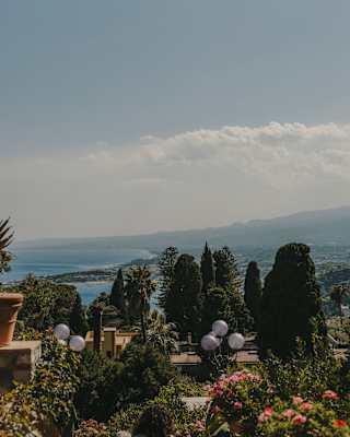 View over the hotel garden's rustic mix of flowering shrubs, pines and potted plants, down to the coast and blue Ionian sea.