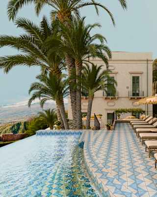 A row of loungers and parasols sit on Villa Timeo's blue and white-tiled terrace by an infinity pool with priceless views.