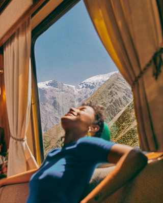 A female guest in a blue top basks in sunshine from the window behind her, which has views onto the incredible Andean peaks.