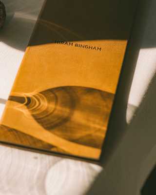 The refracted shadow of a wineglass creates pretty patterns on a closed, tan-covered Hiram Bingham-branded menu.