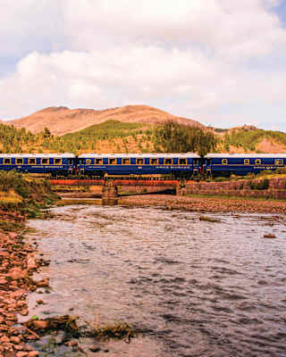 Royal blue train carriages stretching across a bridge over a rocky river