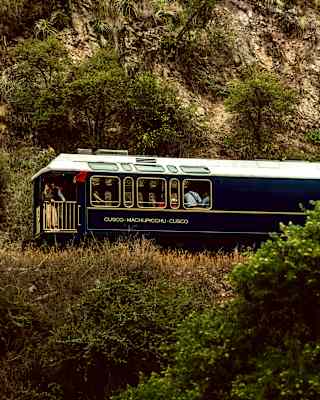 The Observation car, packed with people, follows the rest of the train on a track through hilly terrain, seen from below.