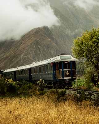 View of the train as it passes in front of a craggy mountain wrapped in cloud, with a glimpse of the Observation Car.