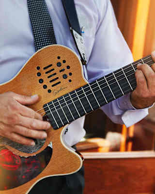Close-up of hands plucking the strings of a wooden electric guitar