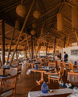 View over Nelayan's terrace where multiple ceiling beams echo the slatted wood dining chairs and plentiful bamboo supports.