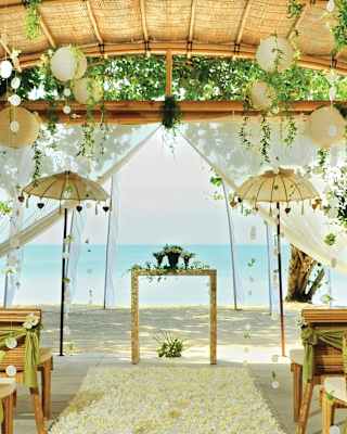 Bamboo pergola over a beach set with rows of chairs and an aisle for a wedding