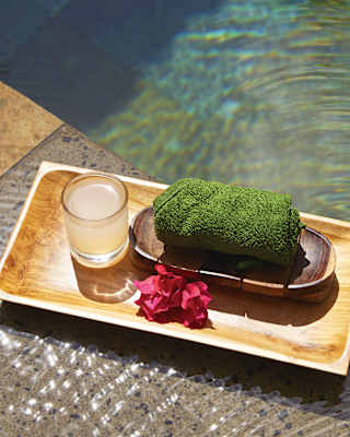 Close-up of a green folded facecloth and a glass of water on a tray beside a pool