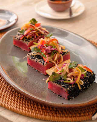 Close-up of a plate with three pieces of seared tuna, coated in sesame-ginger dressing and topped with bright Asian slaw.