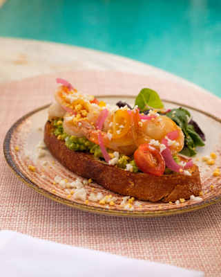 Close-up of a healthy breakfast of avocado toast with feta and tomatoes, served at Corail on a stoneware plate by the pool.