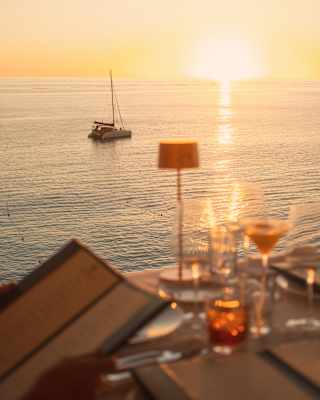 In soft-focus, an off-camera guest peruses the L'Oursin menu at an outside table, as the sun sets on the ocean horizon.