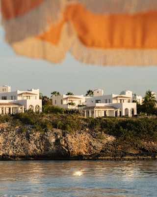 White villas line the clifftops at the south end of Long Beach, seen from beneath the fringe of an orange and white parasol.