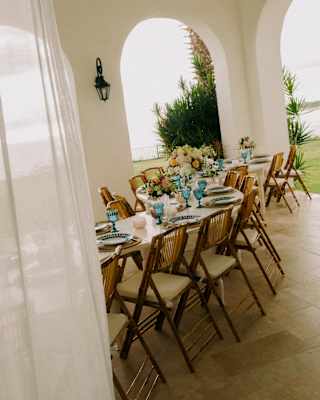 Angled view of a curvy, elegant celebration table on a pool villa terrace, taken from a doorway, part-obscured by a drape.