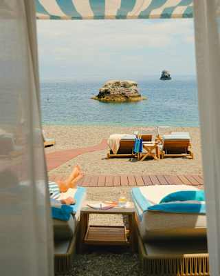 View from a cabana over a sunbather and a pair of vacant beach chairs to the ocean, where two sea stacks jut from the blue.