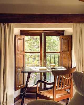 An antique table with turned wooden legs sits in front of a low window with views over the garden's Mediterranean pines