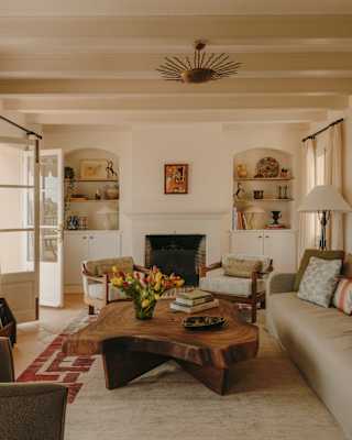 A low table made from a large tree trunk is the centrepiece for a living room with a soft beige sofa and rug and light décor.