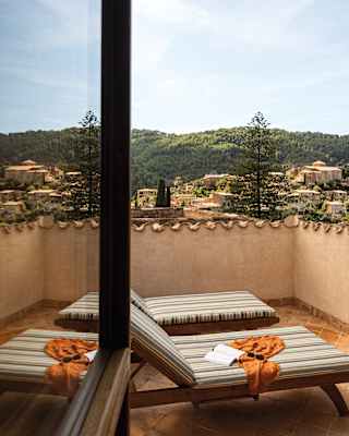 Teak sun loungers with striped cushions and a view over the hillside of Deià are reflected in the glass of an open window