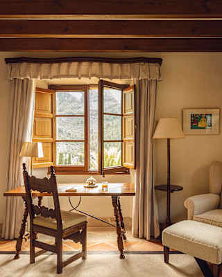 The tree-filled slopes of the Serra de Tramuntana extend high beyond the edge of an open window, beside an antique desk
