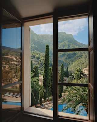 A window's view is like a landscape painting with green mountains touching the sky while palm fronds frame the foreground