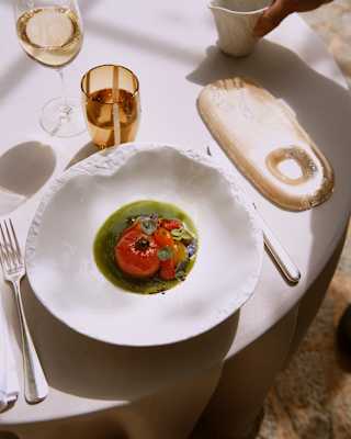 A vibrant vegan appetizer comprises a local Ramallet tomato in green tomato juice with grilled strawberries and black olive.