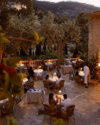 Seen from above, table lamps glow like fireflies during a magical evening on the terrace of El Olivo, circled by gardens.