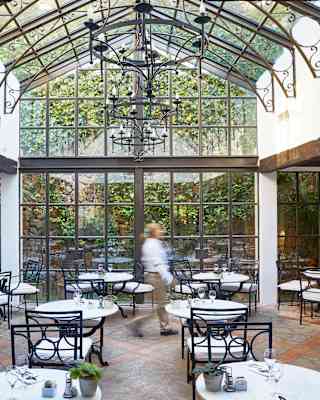 Restaurant with a glass apex ceiling and glass walls surrounded by lush foliage