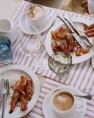 Looking down on a satisfied dining table, where fresh coffees sit by finished plates of prawns and glasses of water and wine.