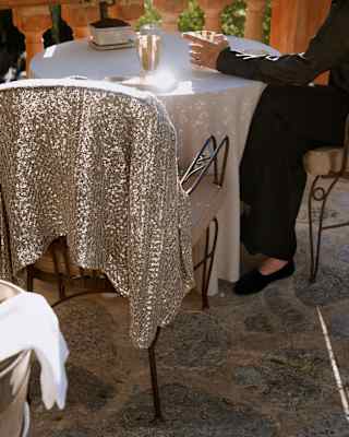 Seen behind a chill bucket, a sequined jacket rests on a chair at a terrace table, where a guest in black drinks Champagne.