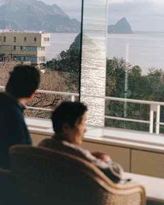 In soft-focus foreground, two men look gaze at Sagami Bay from their hotel window in Atami, photographed by Cecy Young.