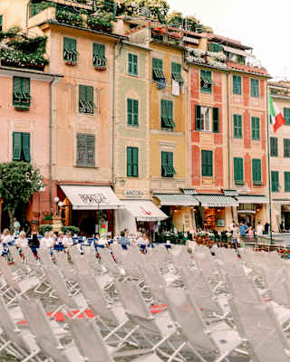 Portofino's buildings, topped with roof gardens and tailed with awnings, seen over rows of white chairs in the La Piazzetta.