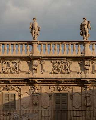 The upper façade of a classical building featuring ornate stone carvings and a balustrade topped with four statues of figures.