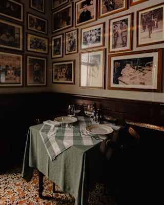 A small dining table set for two with a chequered tablecloth beneath a wall densely decorated with framed vintage photographs.
