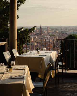 Tables set for dining on a terrace overlooking a city skyline at sunset.