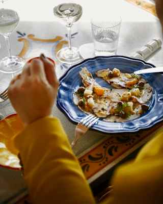 A guest rests her hands on the table by her lunch of focaccia, grilled vegetables and olives, served on a blue china plate.