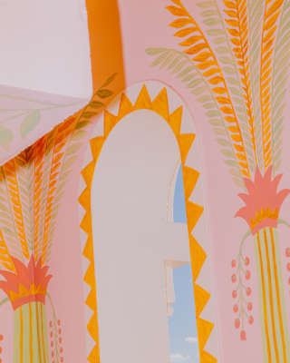 Close-up of a wall arch with a border of hand-painted triangle patterns and palms, done in pinks, oranges, and greens.