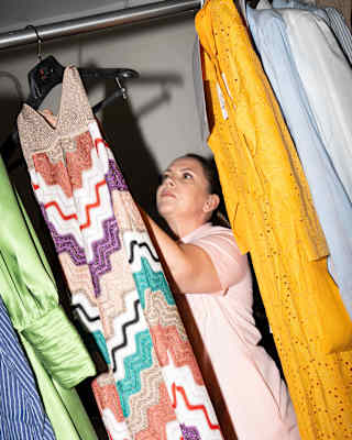 Staff member, Valentina Gentina hangs a laundered long dress with a zig-zag pattern in beige, purple, green, white and red.