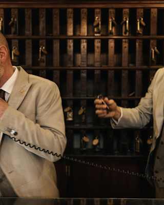A snapshot of hotel reception as one staff member talks on the phone and another holds a room key, both in beige jackets.