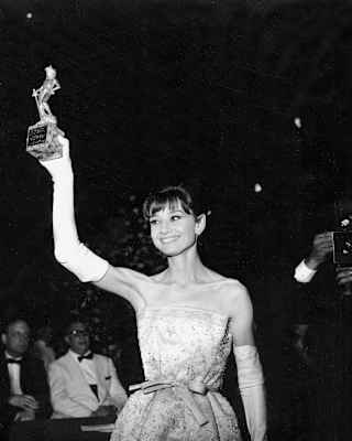 Audrey Hepburn, in long white gloves, holds up her David di Donatello award for best foreign actress, 1960, in monochrome.