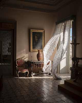 Breeze billows in diaphanous door drapes, bringing sunlight and movement into a darkened, cool room in Palazzo Castellucio.