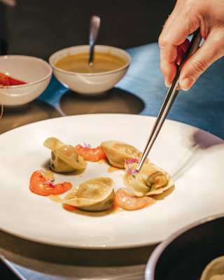 A fine dish of seafood pasta is assembled on a simple white plate on a shiny steel kitchen worktop