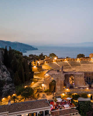 Golden lights dotted around the Teatro Antico di Taormina create a magical arena in the dusk gloom, seen from above.