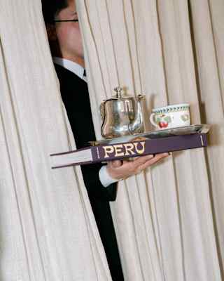 A waiter reaches a hand through a curtain with a copy of Peru flat on their palm, which supports a silver teapot and teacup.